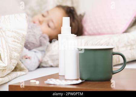 Gros plan vert mug, nez et gorge vaporisateurs contenants et pilules blister sur la table de lit contre le mal défoqué petit enfant, fille dormant dans le lit. Pharm Banque D'Images