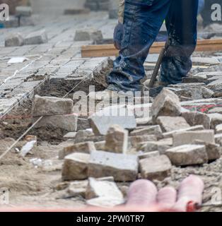 Les travailleurs qui pontent des pavés emboîtés pendant la construction du trottoir avec un sol surélevé rempli de tuyaux et de tuyaux à poser. Banque D'Images