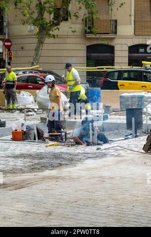 Les travailleurs qui pontent des pavés emboîtés pendant la construction du trottoir avec un sol surélevé rempli de tuyaux et de tuyaux à poser. Banque D'Images