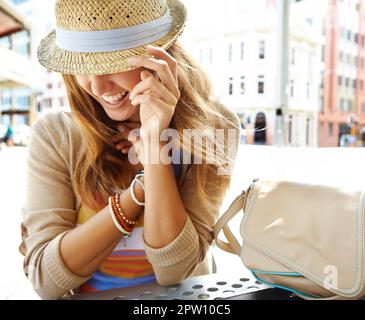 Doux et timide. Une jolie jeune femme portant un chapeau assise dans un café-terrasse de la ville et se cachant sous le bord de son chapeau Banque D'Images