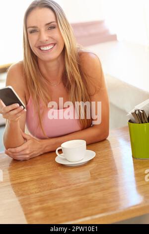 Rester en contact où que je sois. Une belle jeune femme assise dans un café souriant en lisant un message texte Banque D'Images