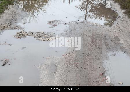 Photo d'un fragment d'une route détruite avec de grandes flaques d'eau par temps de pluie Banque D'Images