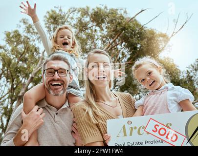 Portrait d'une famille caucasienne heureuse tenant une affiche vendue tout en déménageant et en déménageant dans une nouvelle maison. Les parents souriants et les enfants sûr prêt de propriétaire de maison pour Banque D'Images
