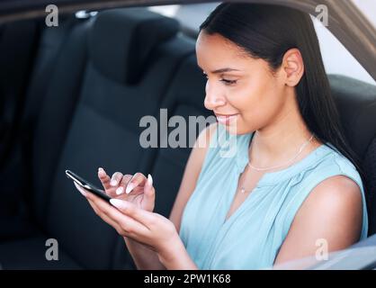 Une jeune femme d'affaires de race mixte tapant un message sur un téléphone tout en étant assise dans une voiture. Bonne femme hispanique utilisant les médias sociaux tout en tenant Banque D'Images
