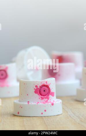 Plusieurs buses en plastique à partir d'un pulvérisateur de peinture qui se trouvent sur une surface en bois contre un mur gris. Les bouchons sont enduites de peinture rose. La conc Banque D'Images