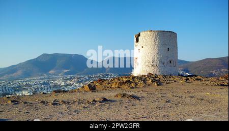 Ruines d'un moulin à vent cassé sur une colline surplombant une ville entourée de montagnes. Murs en ruines de la tour du phare abandonnée. Un blanc arrondi abîmé Banque D'Images