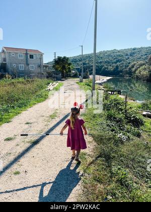 Une petite fille avec des oreilles Minnie Mouse sur sa tête et un filet d'atterrissage dans ses mains marche le long de la rive de la rivière Banque D'Images