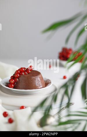 Dessert Panna Cotta au chocolat décoré de raisins de Corinthe rouges sur fond blanc Banque D'Images