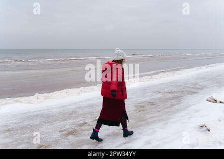 Une femme vêtue de chaleur marche le long de la mer en hiver. Banque D'Images