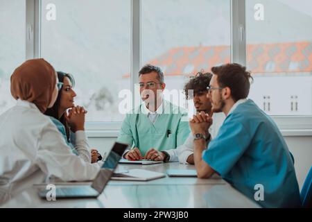 Un groupe de professionnels de la santé multiethniques, y compris des médecins, des chirurgiens et des infirmières, est rassemblé dans un milieu hospitalier pour discuter des soins aux patients et Banque D'Images