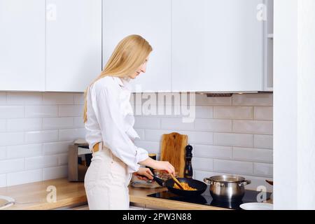 Une femme mignonne braque des légumes dans une poêle à frire Banque D'Images