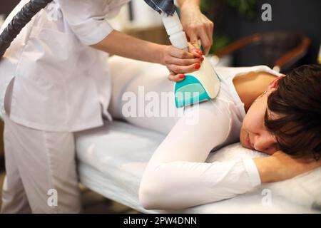 Cosmétique sans visage utilisant un appareil d'amincissement GPL sur le corps de la femme client en costume blanc allongé sur le canapé Banque D'Images