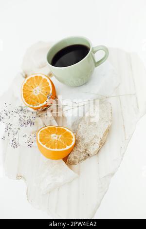 Photo en gros plan du dessus d'une tasse de café noir avec deux moitiés d'oranges coupées sur béton et support en pierre avec branche de fleurs séchées isolées Banque D'Images