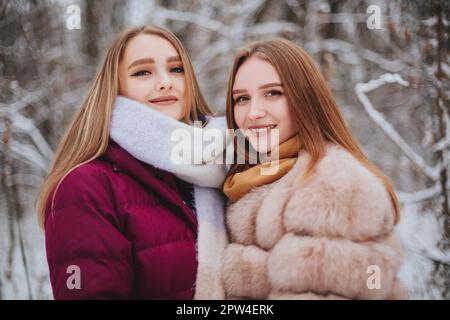 Deux amies joyeuses qui apprécient le temps de neige en plein air, les meilleures amies en hiver vêques en duvet vestes riant et s'amusant en marchant Banque D'Images