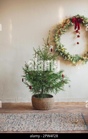 Couronne de Noël élégante ornée d'un noeud rouge et de boules accrochées sur un mur en béton lors des fêtes de Noël Banque D'Images