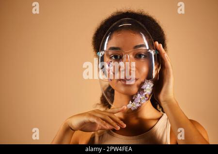 Jeune femme afro-américaine gaie portant un masque de protection en PVC transparent orné de fleurs et regardant la caméra avec des faisceaux Banque D'Images