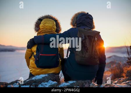 Couple romantique de touristes vêtus de vêtements de sport chauds d'hiver avec des sacs à dos de touristes assis dans les montagnes enneigées dans un incroyable coucher de soleil. Ogoi Banque D'Images