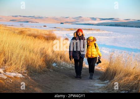 Couple romantique de touristes vêtus de vêtements de sport chauds d'hiver avec des sacs à dos touristiques marchant dans les montagnes enneigées dans un incroyable coucher de soleil. Ogoi Banque D'Images