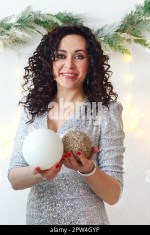 Portrait de bonne humeur positive femme portant la robe de vacances étincelante avec la coiffure festive et le maquillage tenant ornement balles d'arbre de Noël, heureuse femme dedans Banque D'Images