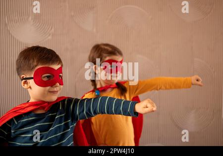 Portrait d'une équipe de deux jeunes super-héros, frère et sœur, sur fond beige. Enfant super-héros. Super héros gamin jouant à la maison. Idée Banque D'Images