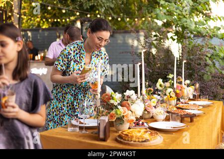 Happy brunette invitée tient un téléphone et prend une photo d'une table de mariage, une photo d'un décor de mariage pour un anniversaire de 20 ans, une fête de jardin Banque D'Images