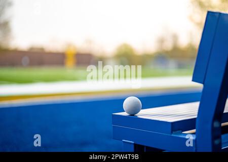 Photo en fin d'après-midi d'une balle de crosse assise sur un siège ou un banc avec un terrain de gazon synthétique en arrière-plan. Banque D'Images