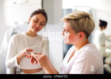 Cosmétique féminine appliquant de la crème hydratante sur les mains du client pendant soin de la peau en salon Banque D'Images