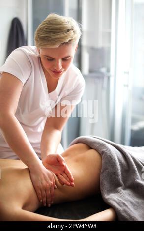 Maître sans visage donnant massage des muscles du dos et des épaules à femme anonyme couchée sur une table dans un salon de spa Banque D'Images