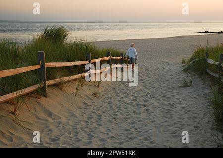 Une femme âgée marche seule le long d'un chemin à travers les dunes vers la mer au coucher du soleil Banque D'Images