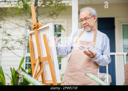 Style de vie les personnes âgées sourire peinture à son chevalet à l'extérieur de la maison, asiatique senior vieux homme peinture image en utilisant la brosse et la couleur de l'huile sur la toile, heureux retir Banque D'Images