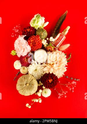 Ensemble de produits cosmétiques naturels, crème pour le visage et bouteille compte-gouttes à l'huile essentielle sur fond rouge avec fleurs colorées, image plate. Soin de la peau Banque D'Images