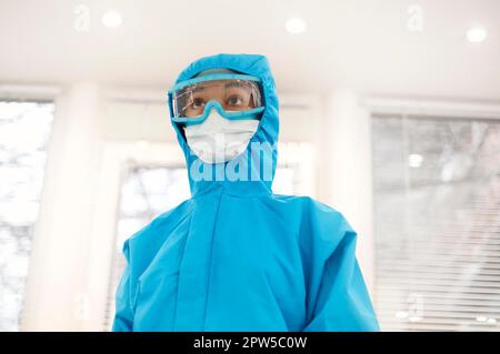 Portrait d'un jeune travailleur médical afro-américain fatigué ou d'une infirmière dans un équipement de protection et un masque facial et regardant la caméra avec une expression frustrée. Banque D'Images
