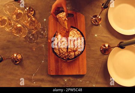 Photo du dessus de la femelle tenant une tranche de gâteau panettone frais couché sur une planche à découper en bois sur la table, servi pour un dîner de fête avec propre Banque D'Images