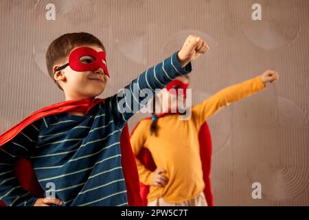 Portrait d'une équipe de deux jeunes super-héros, frère et sœur, sur fond beige. Enfant super-héros. Super héros gamin jouant à la maison. Idée Banque D'Images