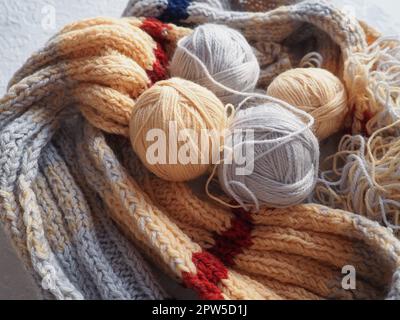 Tricoter une écharpe ou un chandail en fils gris, beige et orange. Billes de laine et de fils acryliques. Tricoter comme un passe-temps. Accessoires, aiguilles à tricoter Banque D'Images