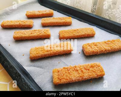 Les bâtonnets de poisson congelés sont disposés sur du papier de cuisson. Cuisson d'une spécialité de poisson. Papier de cuisson sur une plaque de cuisson. Un déjeuner rapide du four. Menu poisson. Réparer Banque D'Images