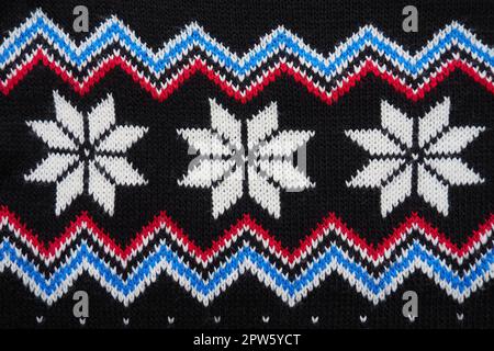 Motif jacquard tricoté. Décoration géométrique pour Noël ou nouvel an. Flocons de neige blancs tricotés, zigzag bleu, points sur fond noir. Jachère d'hiver Banque D'Images