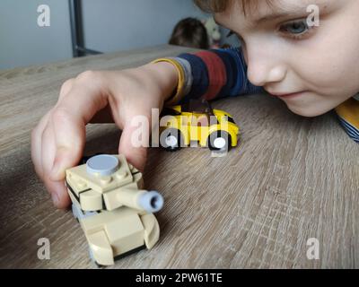 Char à jouets sur une table en bois. Jouet en plastique. Artisanat d'un concepteur pour enfants. Couleur beige du réservoir, image défocuée. Visage et main d'un enfant. Banque D'Images