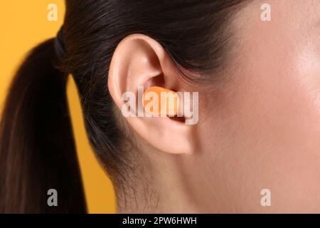 Jeune femme portant un bouchon d'oreille en mousse sur fond jaune, gros plan Banque D'Images