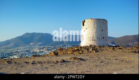 Ruines d'un moulin à vent cassé sur une colline surplombant une ville entourée de montagnes. Murs en ruines de la tour du phare abandonnée. Un blanc arrondi abîmé Banque D'Images