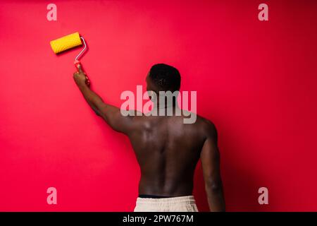 Un peintre africain s'est concentré sur le travail tenant un rouleau professionnel pour peindre un mur intérieur, studio. Banque D'Images