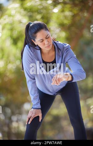 Fitness, fatiguée et femme avec une montre intelligente au parc pour le temps de course, la performance et l'exercice cardio en plein air. Le coureur femelle vérifie le chronomètre, l'horloge et Banque D'Images