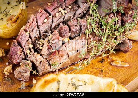 CÔTÉ STEAK bœuf barbecue. Viande rôtie aux pommes de terre et au thym sur une planche de bois, entièrement coupée en tranches. Banque D'Images