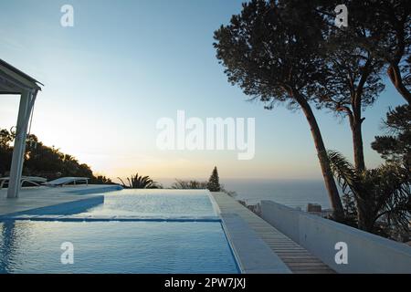 Vue panoramique au coucher du soleil sur une piscine à débordement avec fond d'océan. Piscine extérieure de luxe sur une terrasse, patio, toit d'un appartement, maison, hôtel Banque D'Images