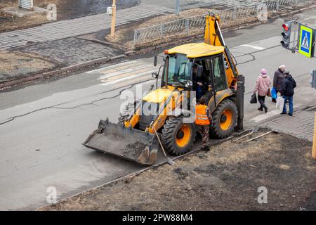 26.04.2023, Kemerovo, Russie. Un tracteur jaune est debout ou conduit sur la route pour les travaux sur route. Nettoyage de la rue avec un tracteur Banque D'Images