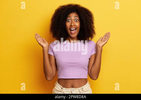 Surprise femme aux cheveux maurs souriant édenté avec une large bouche ouverte, distribue les paumes de côté, posant sur fond jaune. Photo de haute qualité Banque D'Images