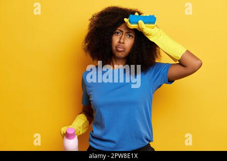 Femme afro-américaine fatiguée après un dur processus de nettoyage, elle met sa main sur sa tête et respire avec le visage fatigué. Banque D'Images