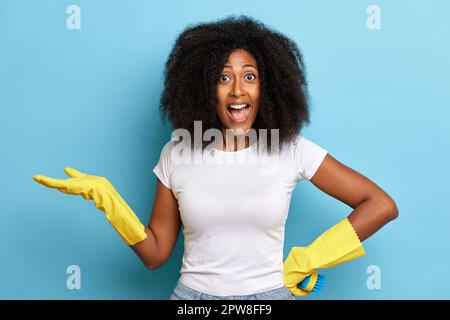 Portrait de brunette émotive housemaid, se reposant après le nettoyage de la maison et regardant avec le visage excité dans l'appareil photo, isolé sur fond bleu. Haute qu Banque D'Images