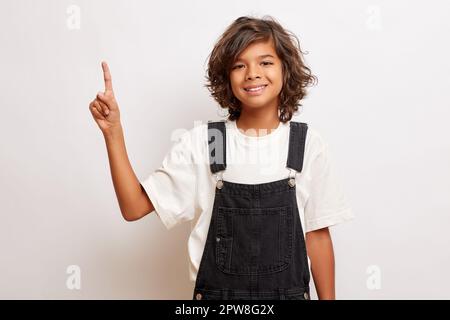 Mignon brunette maurily cheveux jeune gars points index doigt à l'espace vide pour votre publicité, sourires heureux, porte le tissu décontracté. Concep promotionnel Banque D'Images