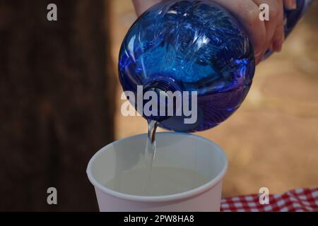 Verser de l'eau claire en bouteille dans une tasse en papier blanc Banque D'Images